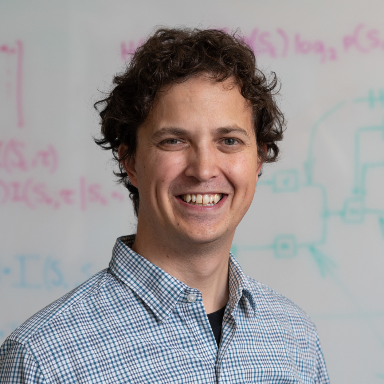 Simon Sponberg smiling in front of a whiteboard with equations and diagrams on it.